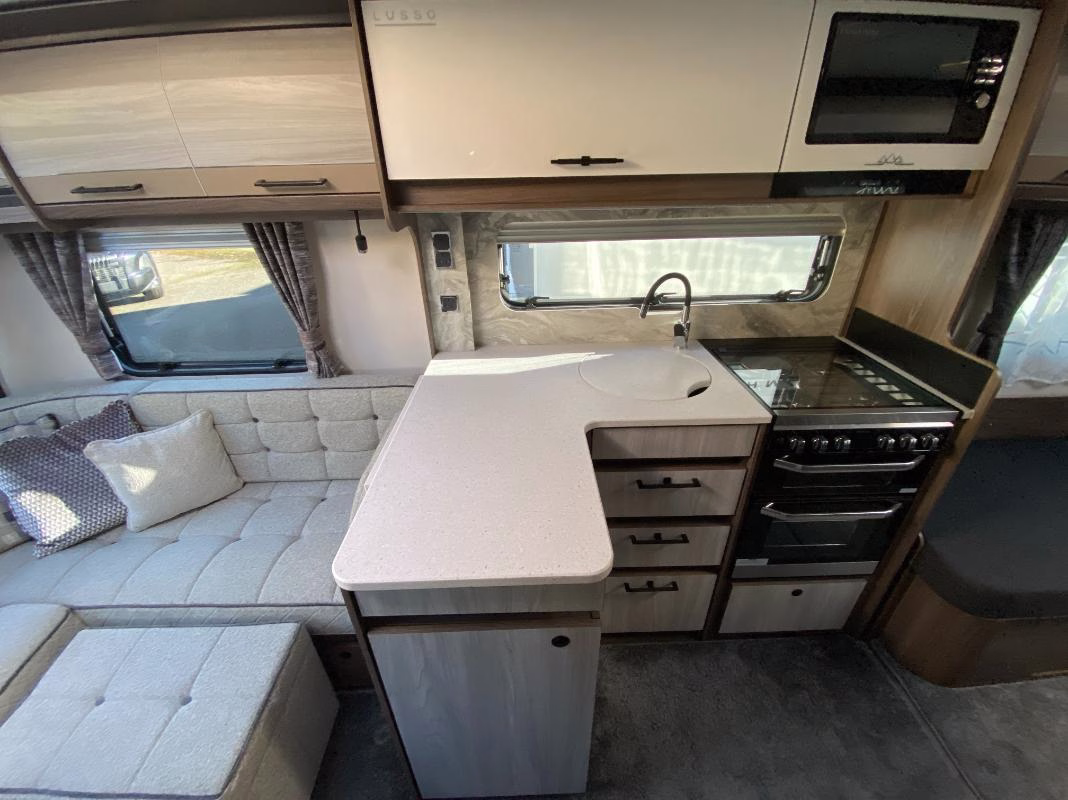 Compact kitchen area in the 2025 Coachman Lusso III featuring a countertop with sink, stove, oven, and overhead storage cabinets