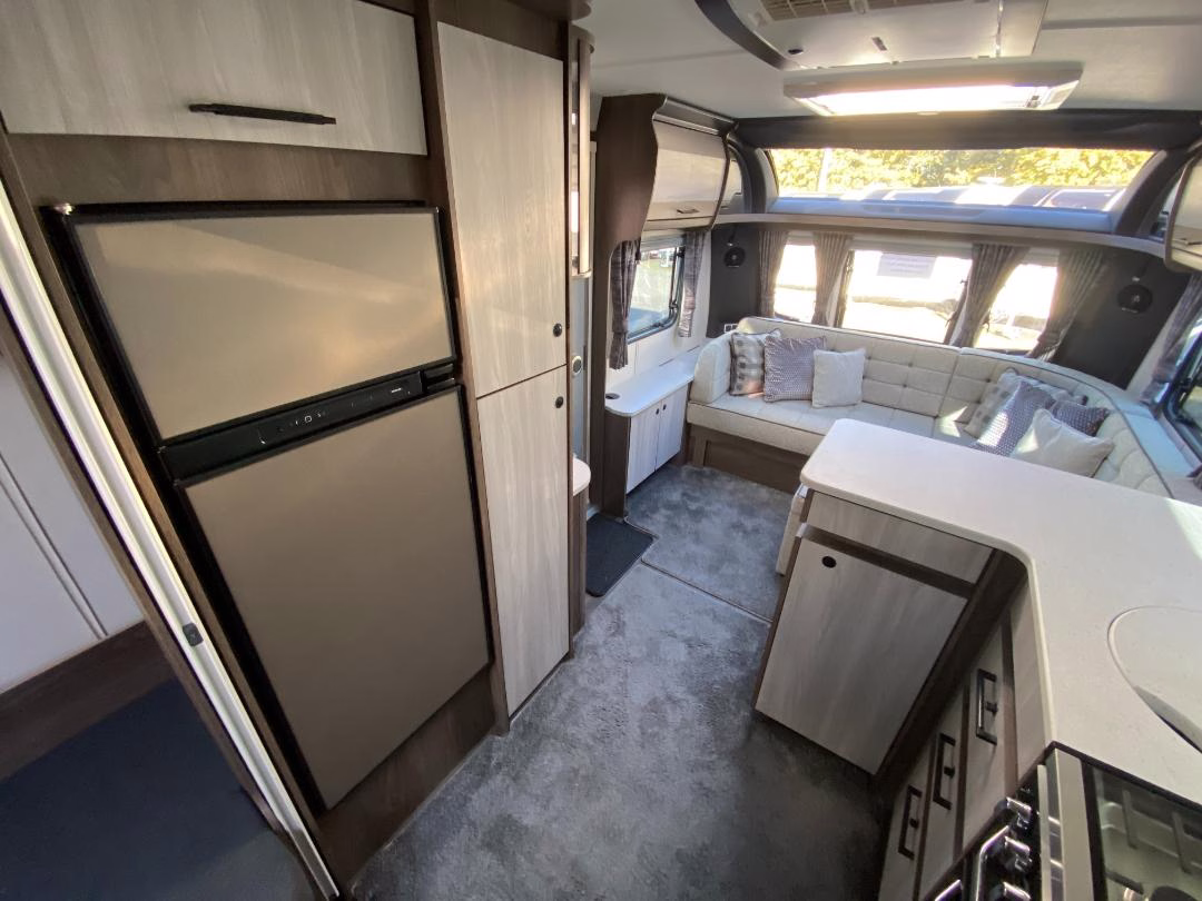 Interior view of the 2025 Coachman Lusso III showing kitchen appliances and a cushioned seating area with windows and curtains