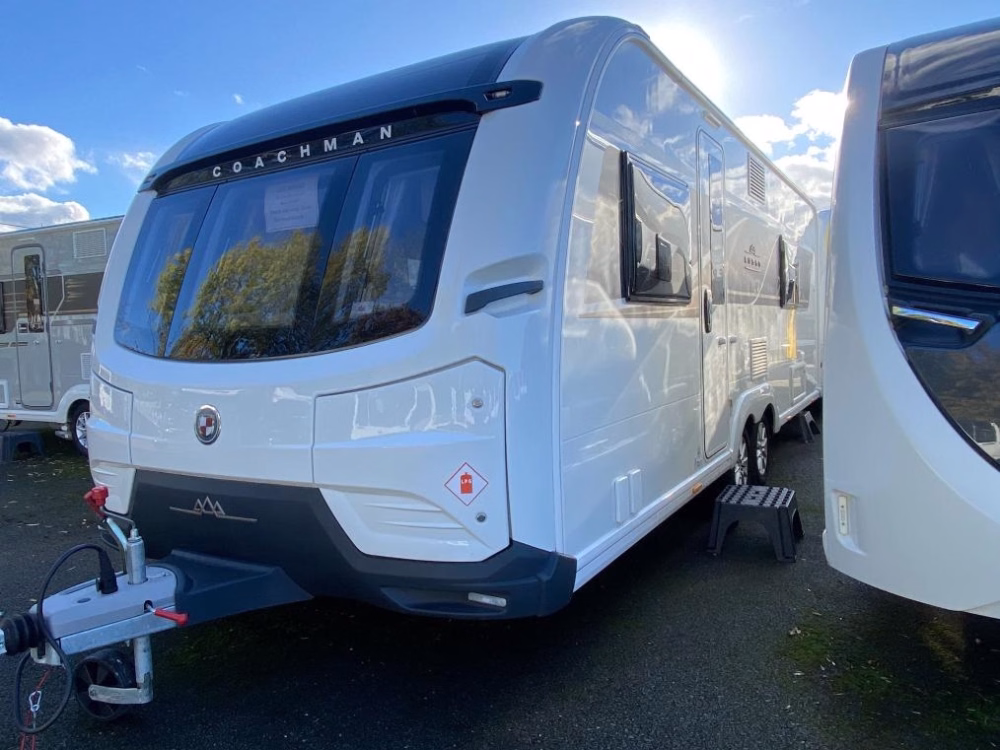 Shiny white 2025 Coachman Lusso III caravan parked outside under a blue sky, showcasing its modern design and large front windows